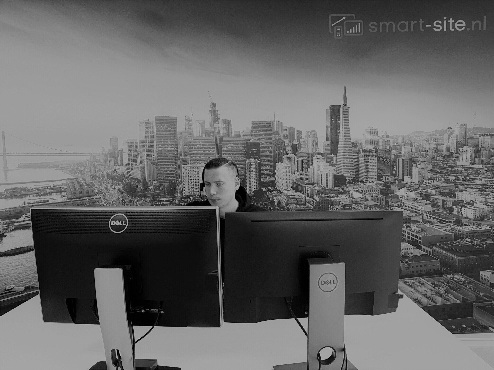 A man is sitting in front of two dell computer monitors.