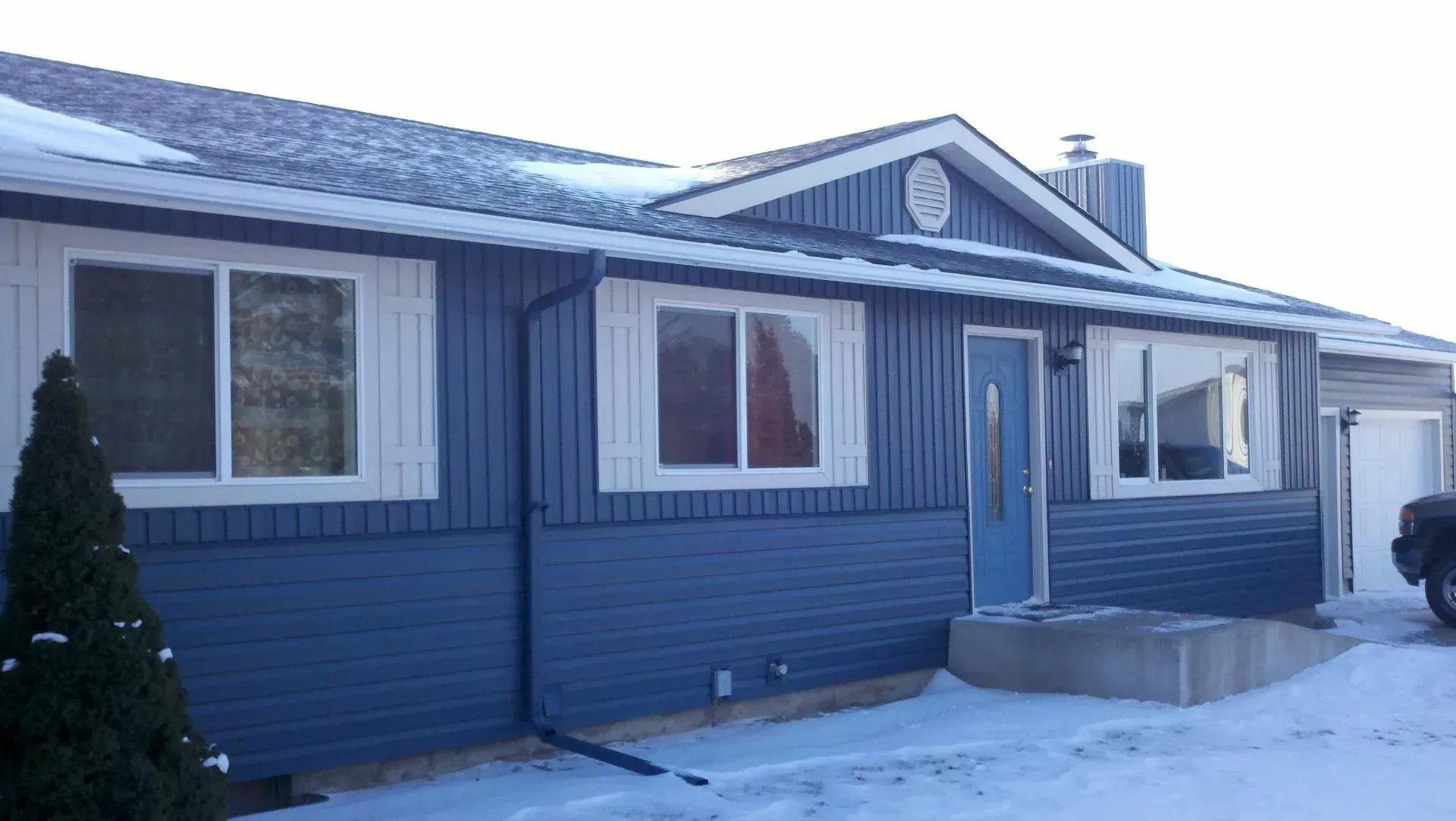 A blue house with white windows is covered in snow.