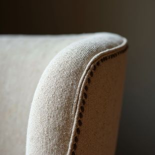 Curved beige chair back with dark stitching detail, against a neutral backdrop.