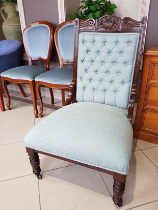 Antique button-tufted chair with light blue upholstery, ornate back, and carved legs, next to similar chairs.