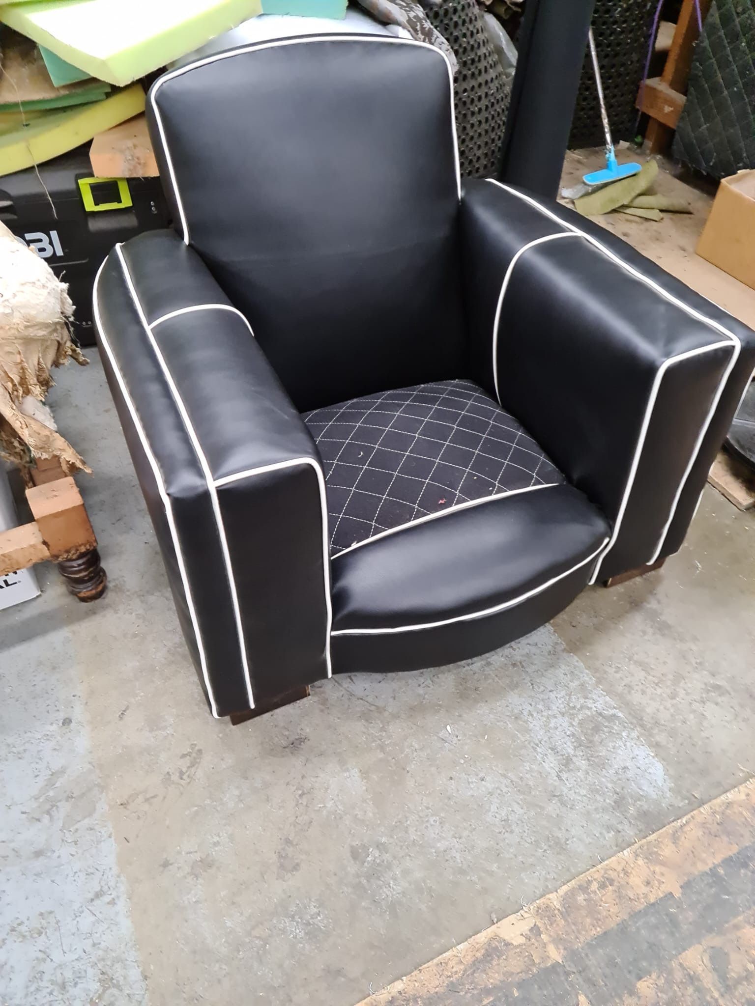 Black armchair with white piping and diamond-stitched seat, in a workshop setting.