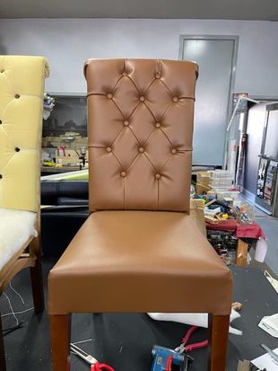 Brown leather button-tufted dining chair with wooden legs, in a workshop setting.