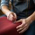 Person using a sewing machine, stitching red fabric, wearing denim apron.