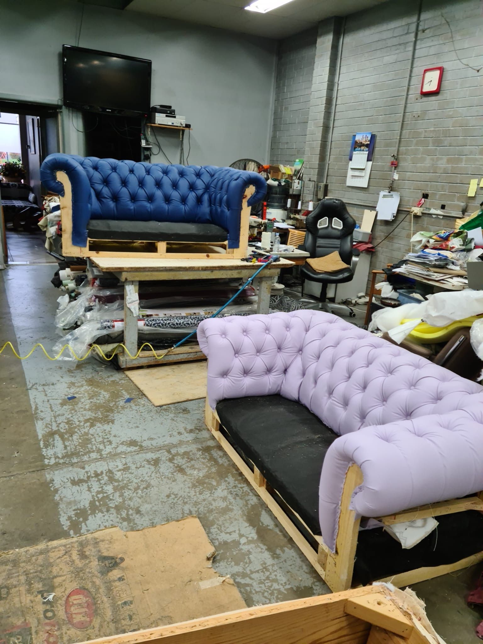 Two tufted sofas, one blue, one purple, in a workshop.