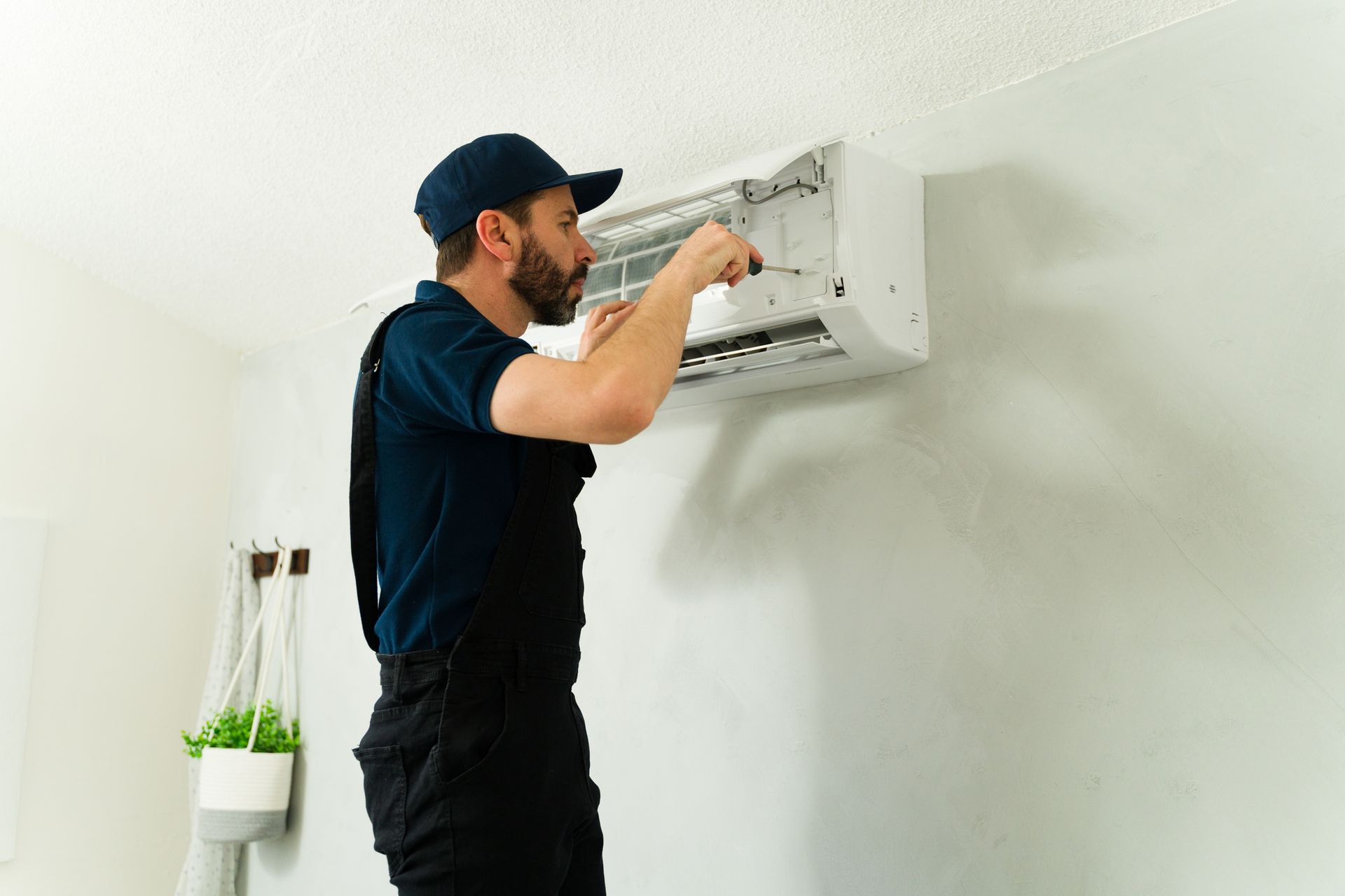 Un technicien nettoie un climatiseur mural dans une pièce d'un blanc éclatant.