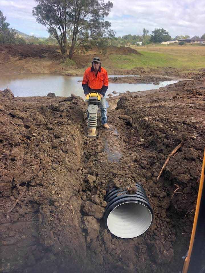 A Man Is Standing In The Dirt Next To A Pipe — A2Z Property Services In Kybong, QLD