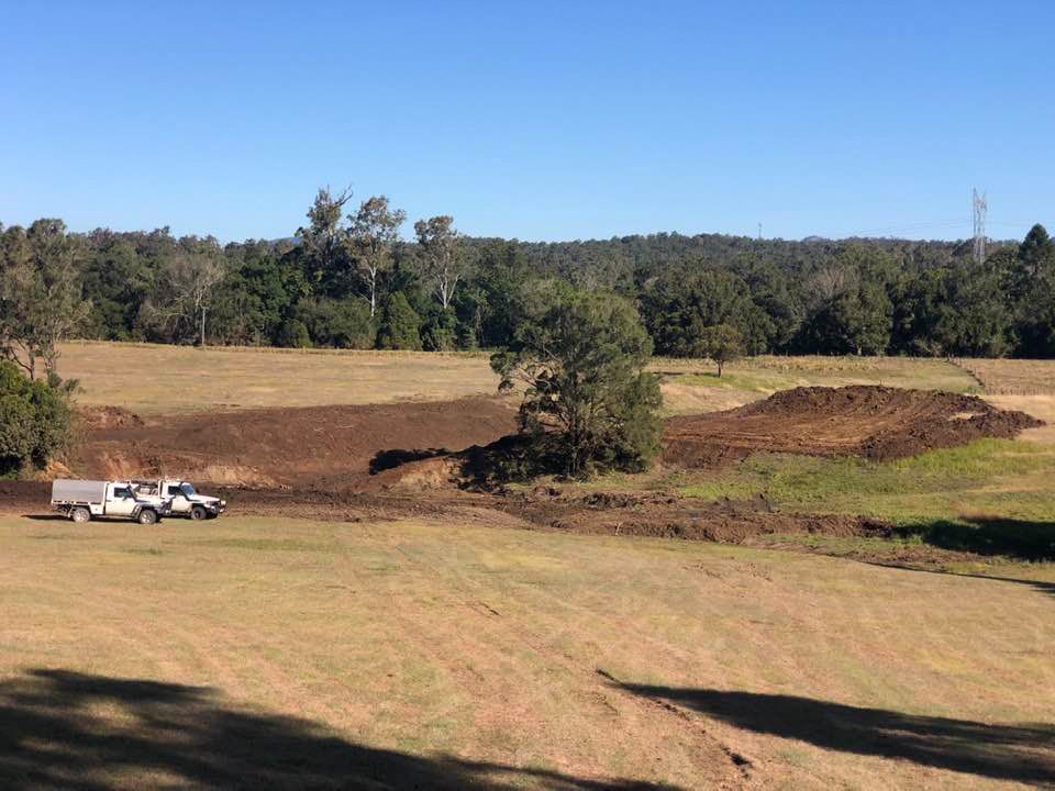 A Large Grassy Field With a Lot of Dirt and Trees in the Background — A2Z Property Services In Kybong, QLD