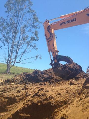 A Yellow Excavator Is Digging A Hole In The Dirt — A2Z Property Services In Cooroy, QLD
