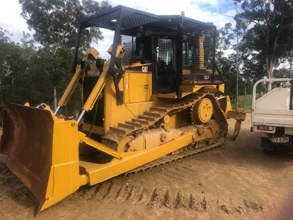 A Yellow Bulldozer is Parked Next to a White Truck — A2Z Property Services In Kybong, QLD