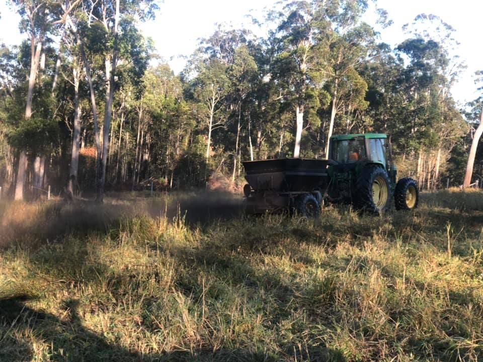 a Green Tractor Spreading Fertilizer in a Grassy Field — A2Z Property Services In Kybong, QLD