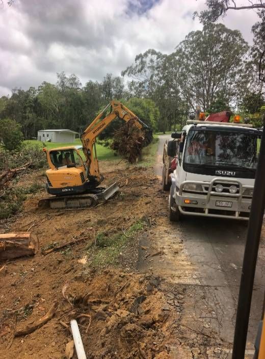 A Truck Is Driving Down A Dirt Road Next To A Yellow Excavator — A2Z Property Services In Kilkivan, QLD