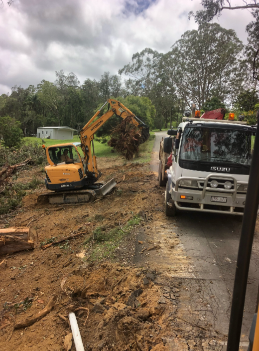 A Truck Is Driving Down A Dirt Road Next To A Yellow Excavator — A2Z Property Services In Gympie, QLD