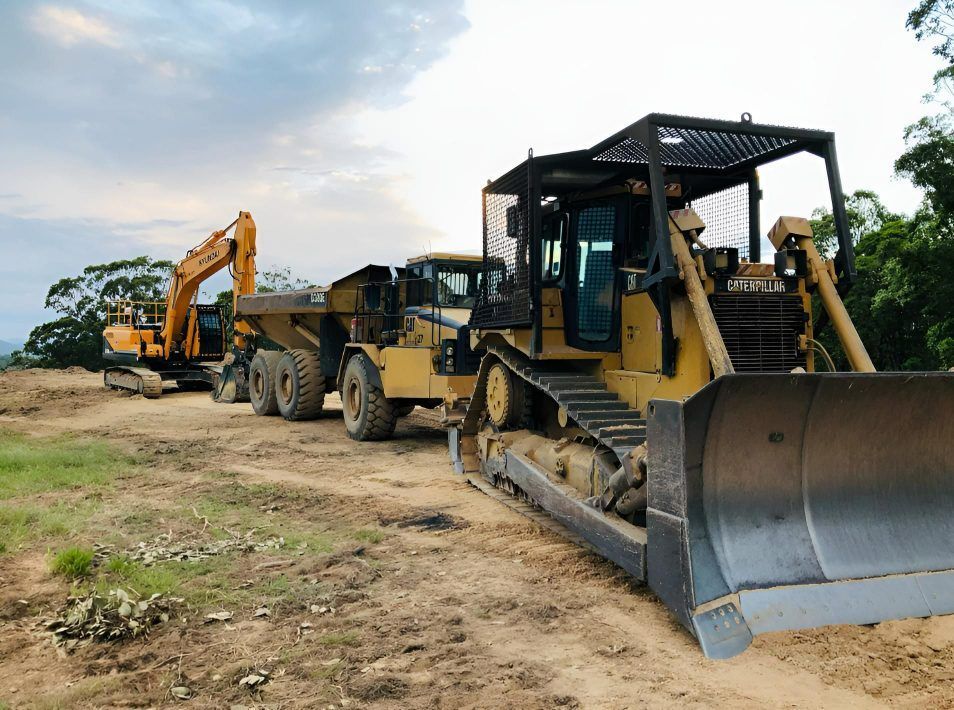 A Yellow Excavator On A Dirt Driveway With A Yellow Truck Behind It — A2Z Property Services In Kybong, QLD