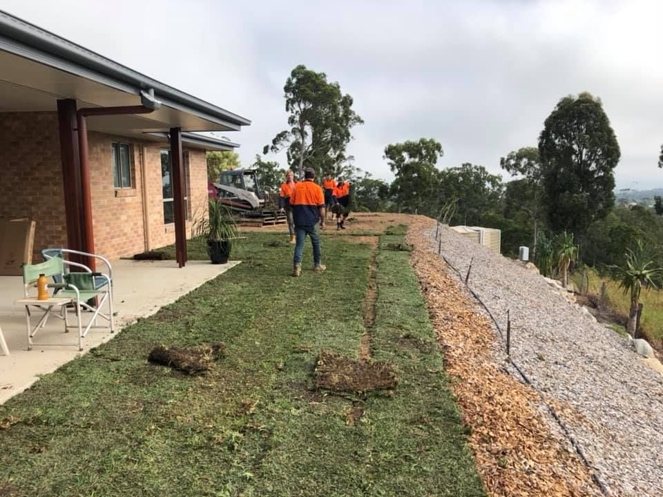 A Workers Laying Sod on A Slope Next to A House — A2Z Property Services In Cooroy, QLD