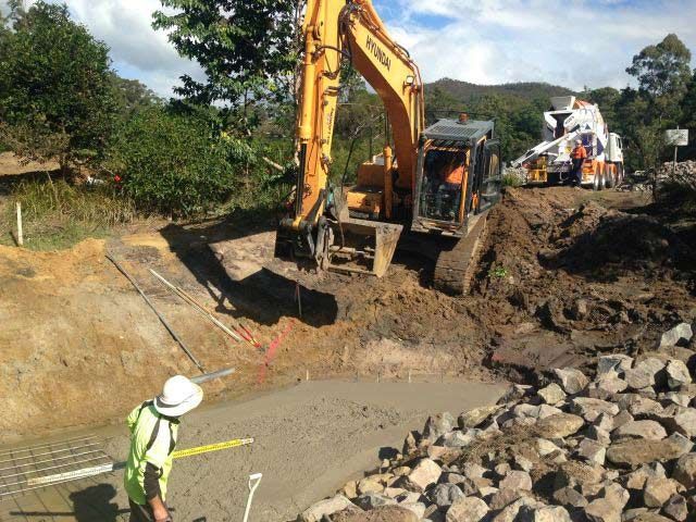 A Yellow Excavator Is Digging In The Dirt Near A Pile Of Rocks — A2Z Property Services In Kybong, QLD