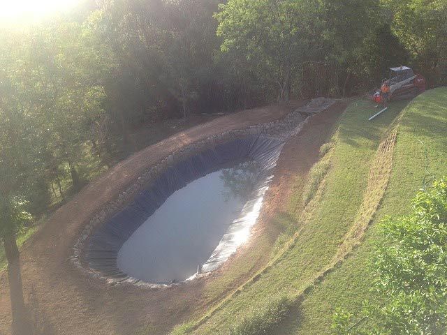 An Aerial View Of A Small Pond In The Middle Of A Field Surrounded By Trees — A2Z Property Services In Kybong, QLD