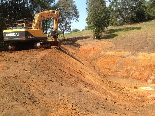 A Yellow Excavator Is Driving Down A Dirt Road — A2Z Property Services In Widgee, QLD