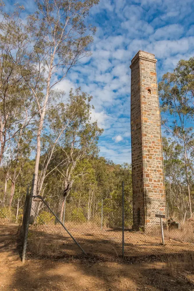 An old brick chimney in the middle of a forest surrounded by trees.