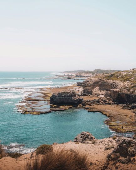 Coastal view with turquoise water, rocky cliffs, and a light blue sky.