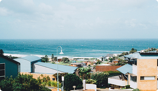 View of houses with ocean in the background, on a sunny day with blue skies.