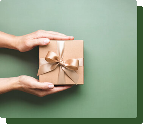 Hands holding a small, wrapped gift box with a gold bow against a green background.