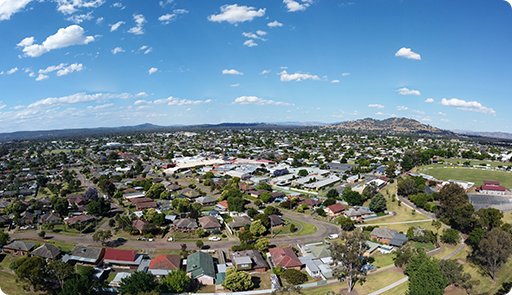 Aerial view of a suburban area with houses, trees, and a large building under a blue sky with clouds.