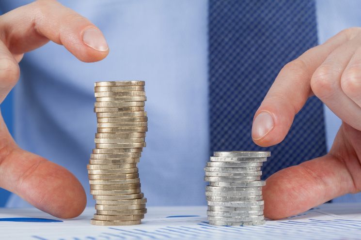 Hands of a person in a blue shirt, framing two uneven stacks of coins, comparing sizes.