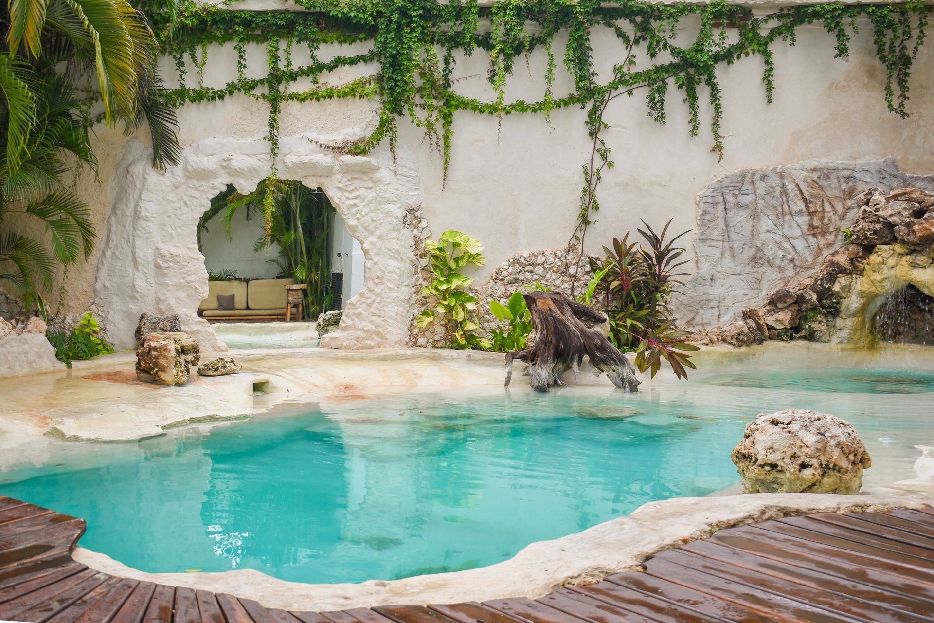 A turquoise pool with stone walls, cascading vines, and a doorway entrance.
