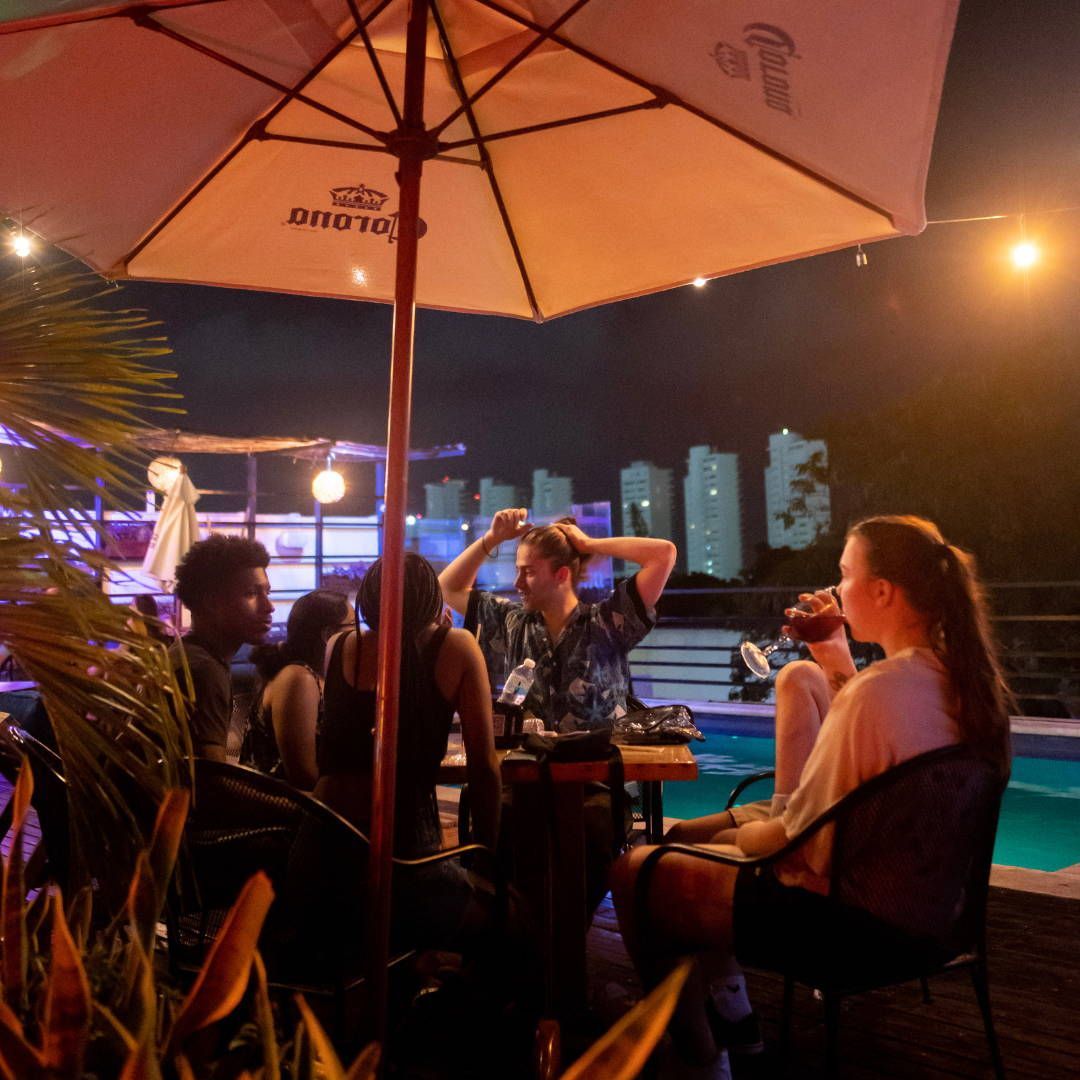 A group of people sit under an umbrella that says corona