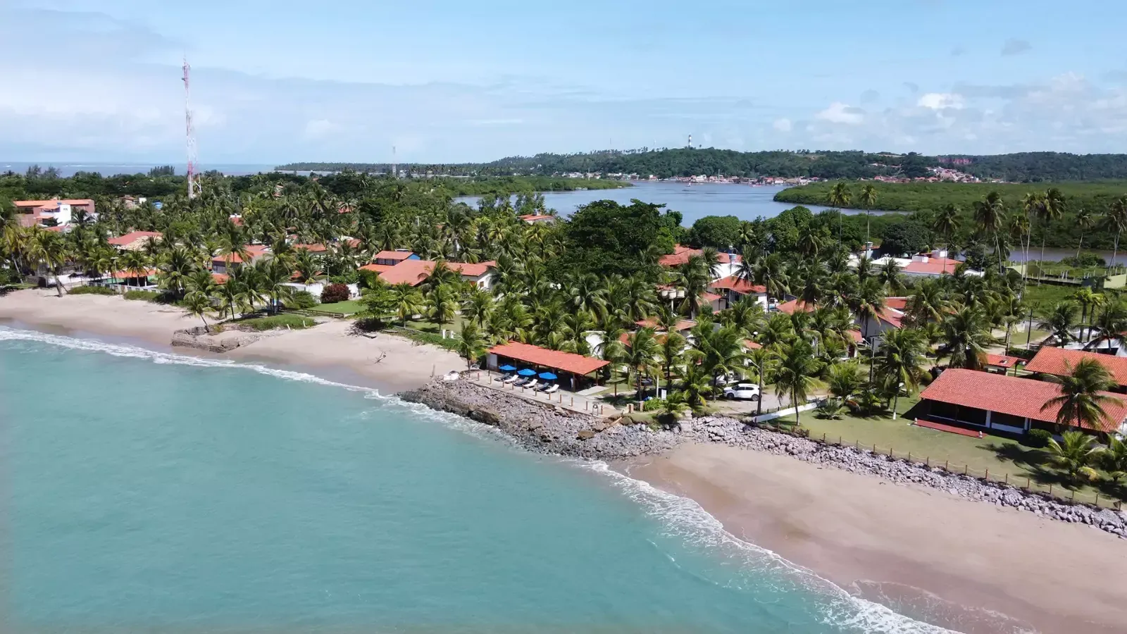 Uma fileira de espreguiçadeiras sob guarda-sóis azuis em uma praia.-Pousada-Bangalos-do-Pontal
