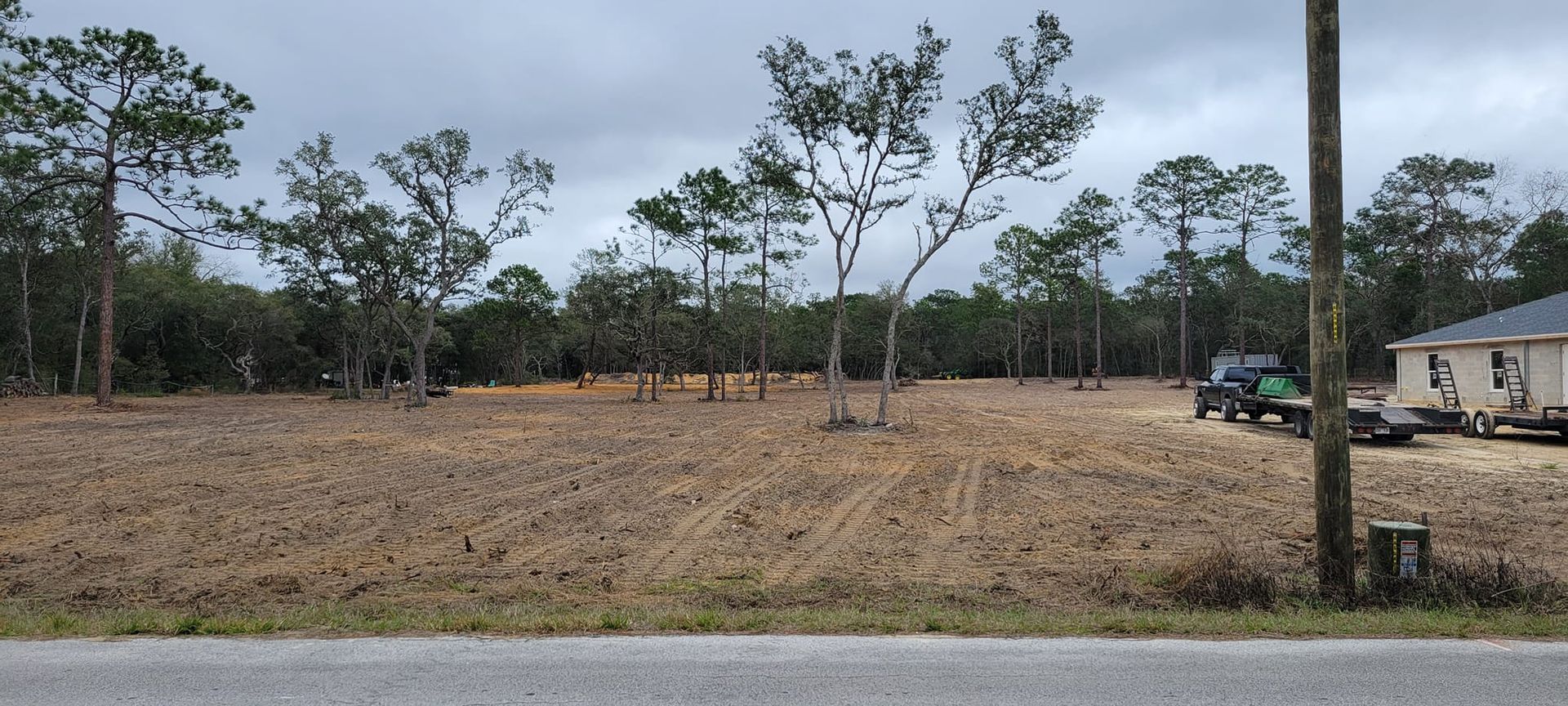 A cleared lot with trees and a tractor, under a cloudy sky. A house is on the right.