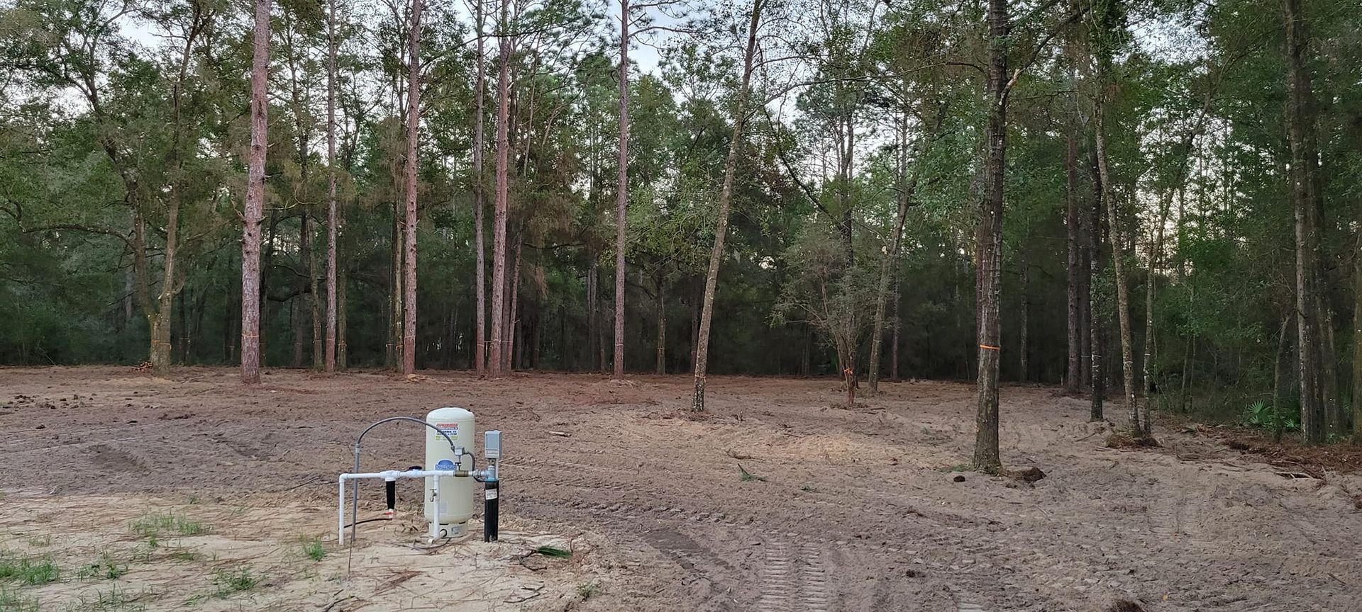 Dirt clearing with trees in the background and a concrete structure in the foreground.