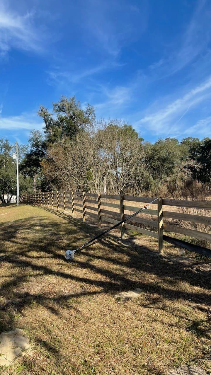 Wooden fence in a sunny field, trees in the background, blue sky with wispy clouds.
