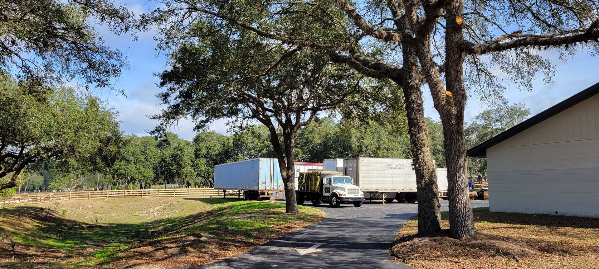 A rural scene with trees, trucks, a building, and a grassy field.