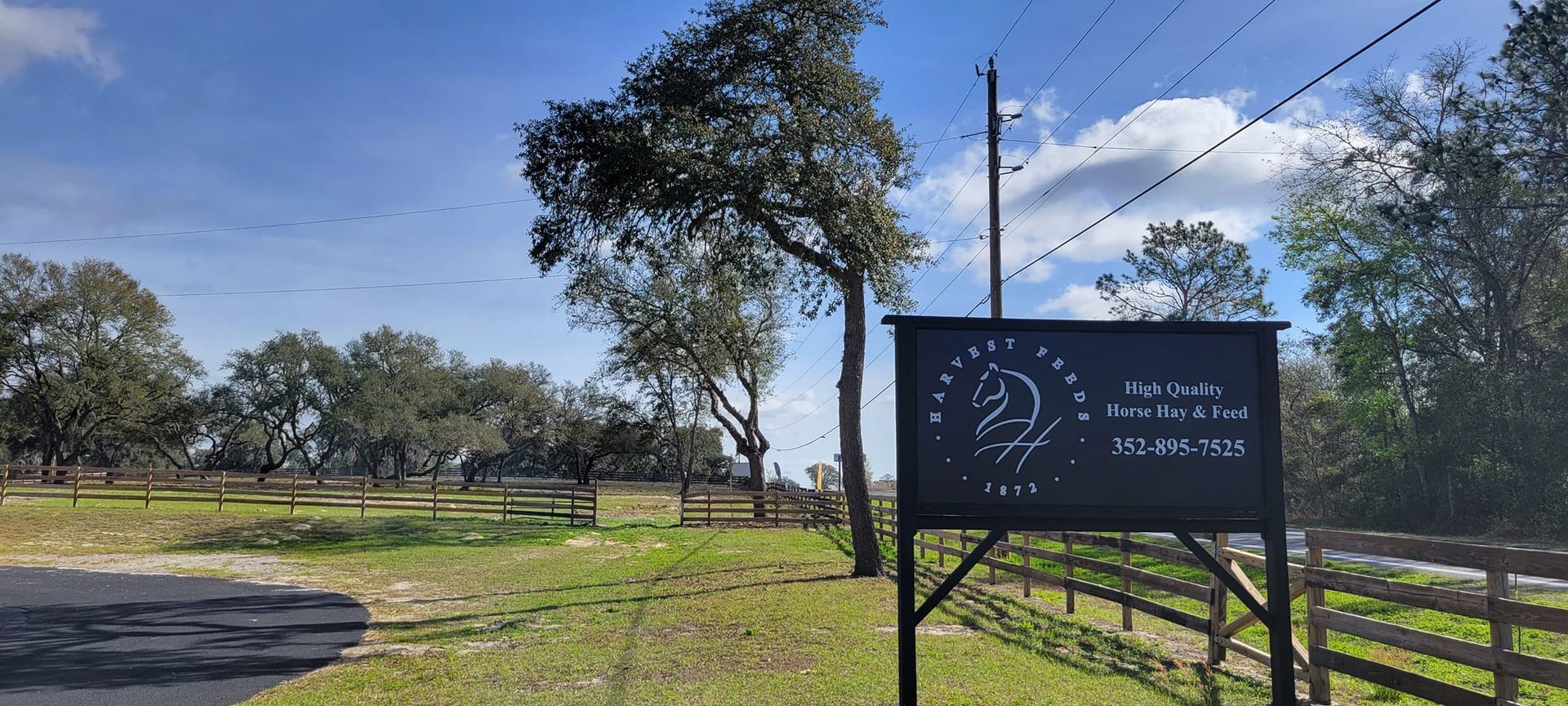 Sign for 'Espada Stables' on a grassy landscape with trees and a cloudy sky.