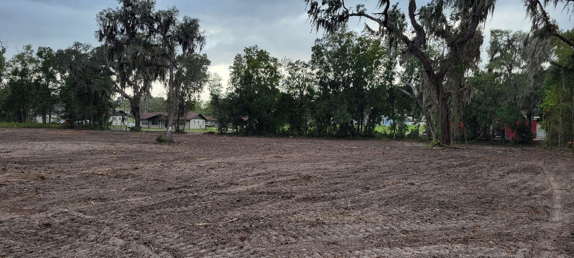 A cleared field with loose soil, trees at the back, and a cloudy sky above.