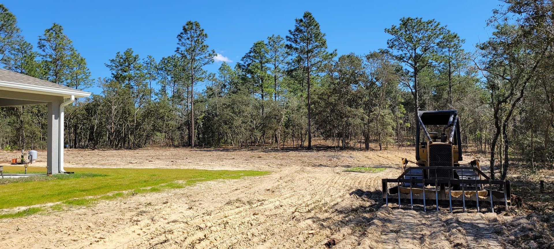 A cleared lot with a small tractor, some trees in the background, and a building on the left.