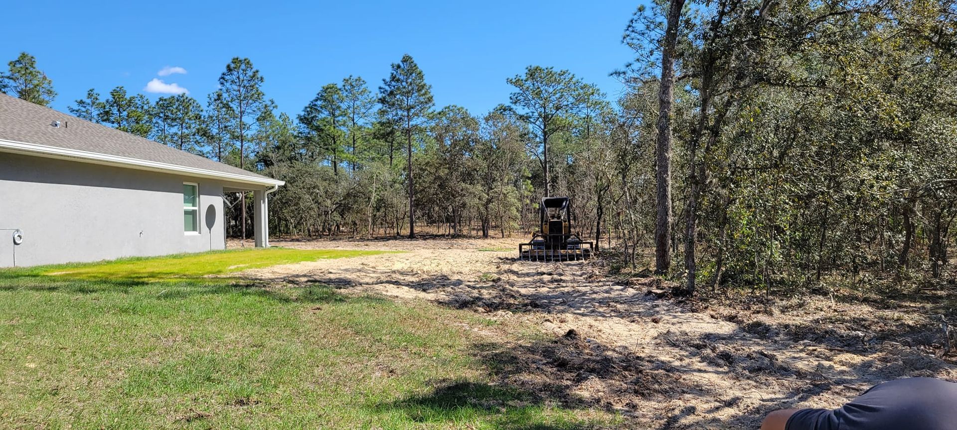 Construction site with a house, cleared land, and equipment. Trees and blue sky in the background.