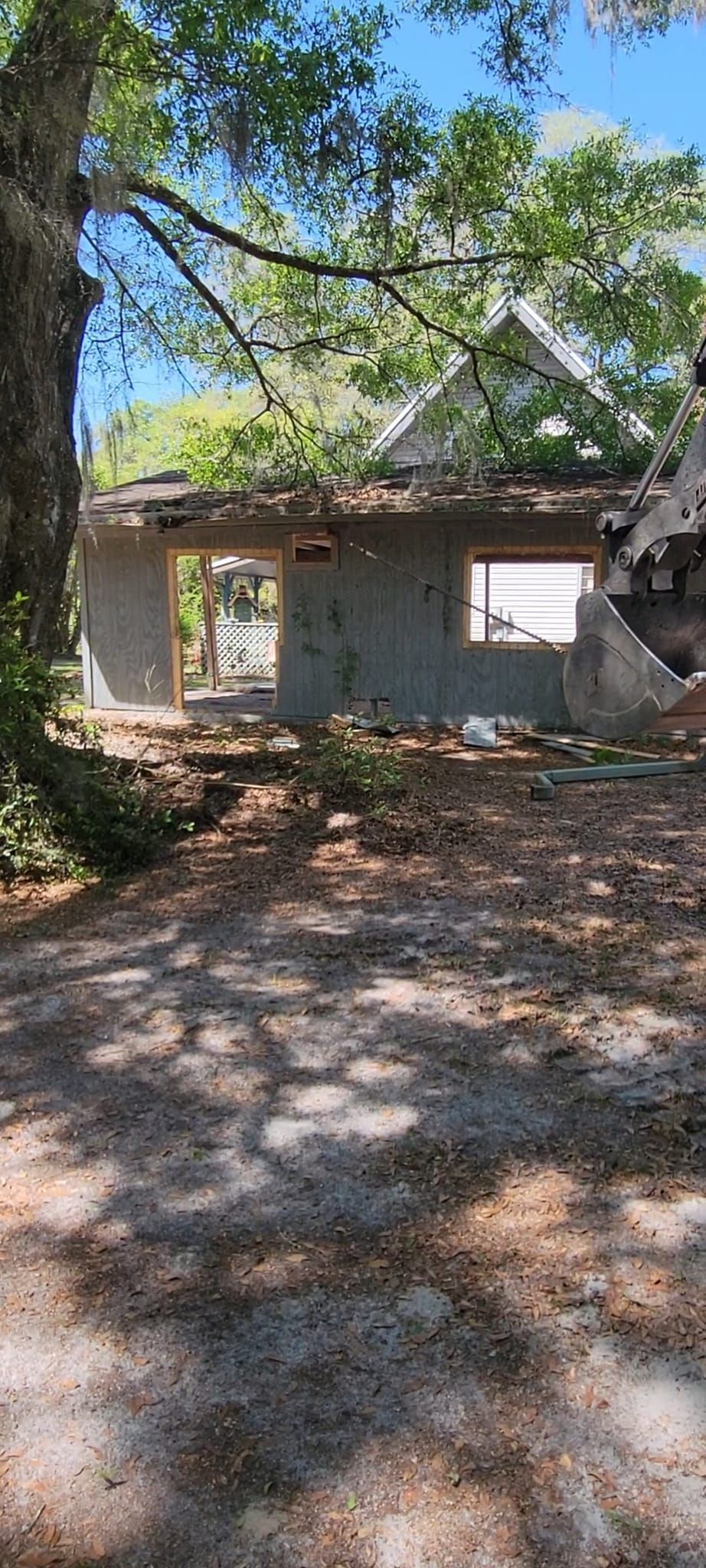 Dilapidated building with missing roof and open windows, framed by trees and a dirt path.