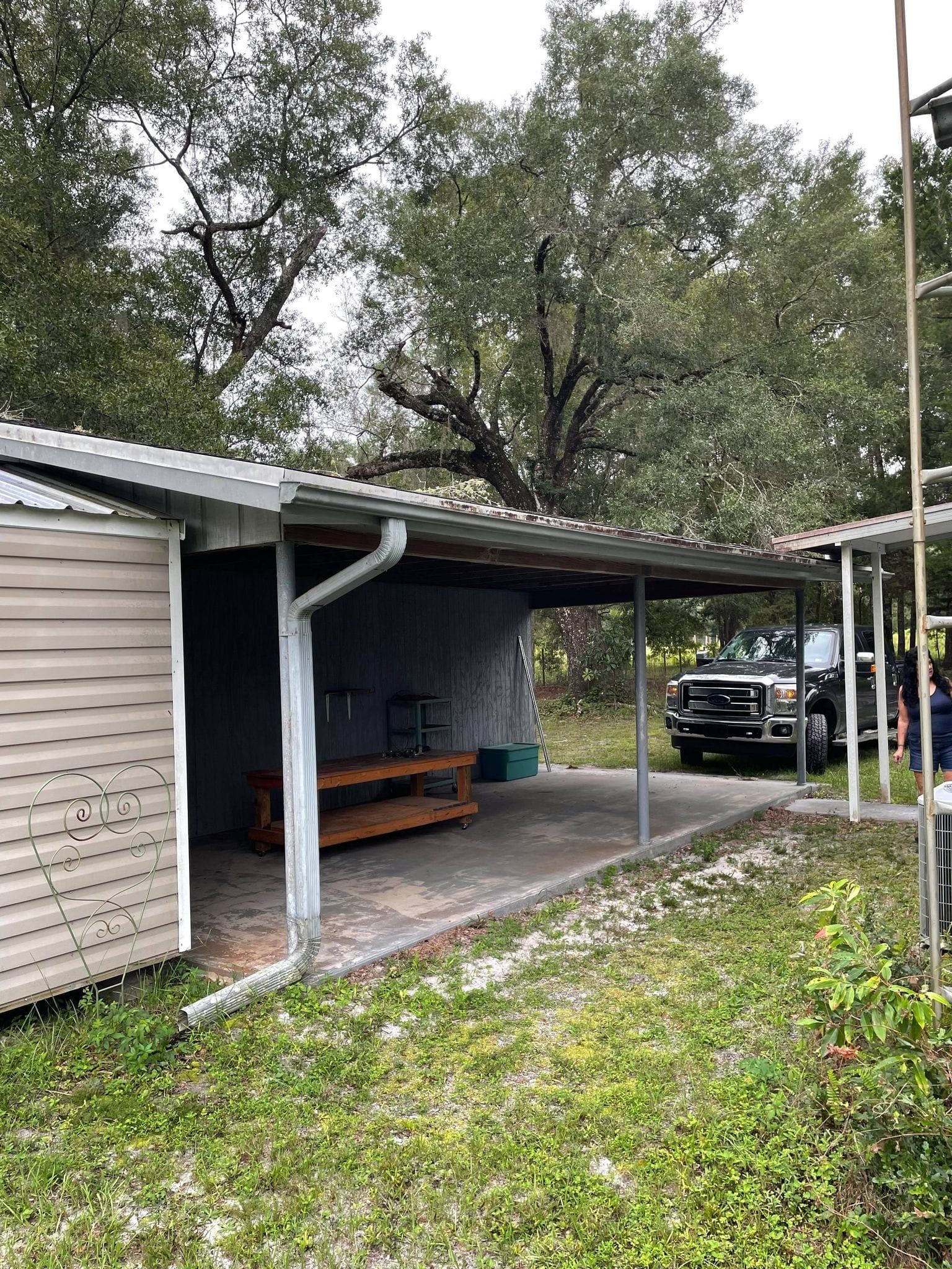 Shed with awning, a pickup truck parked underneath, and surrounding green grassy area.
