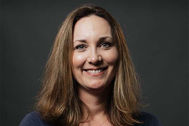 Woman smiling, wearing a blue shirt and white cardigan, outdoors.