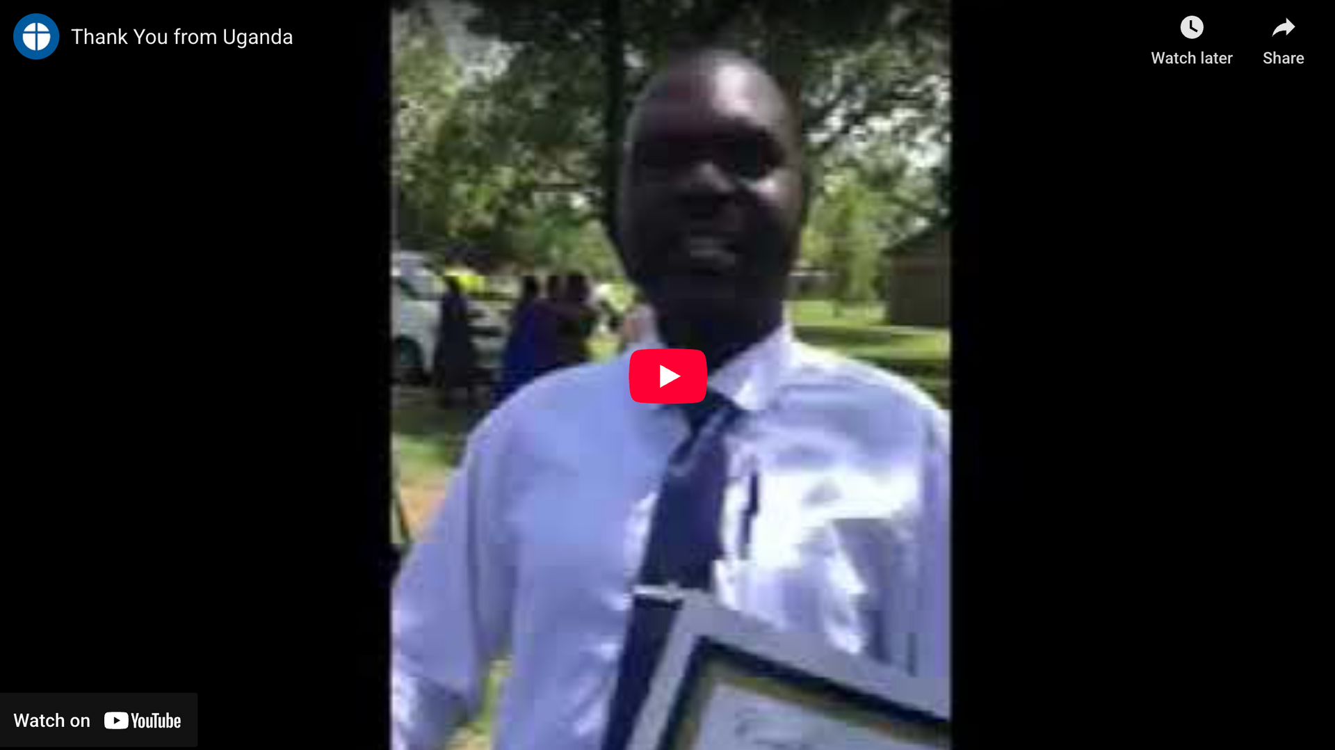Man in a light blue shirt and tie holding a framed certificate outdoors.