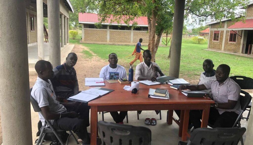 People seated around a table under a covered outdoor area, reviewing documents.