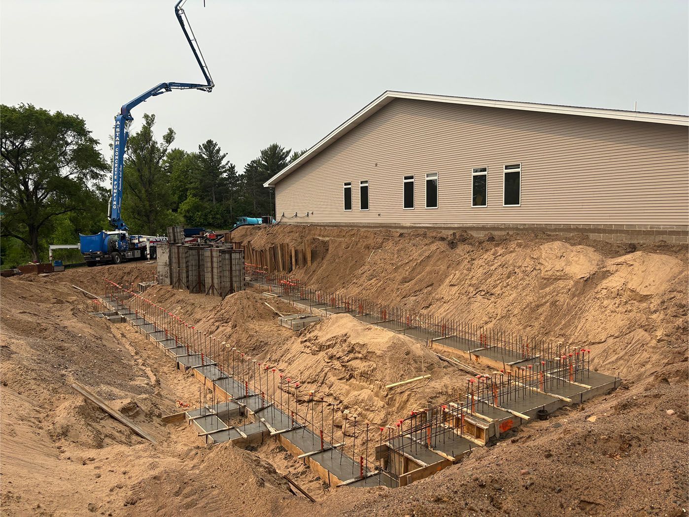 Construction site: concrete foundation being poured. A blue pump truck extends a boom. Building in background.