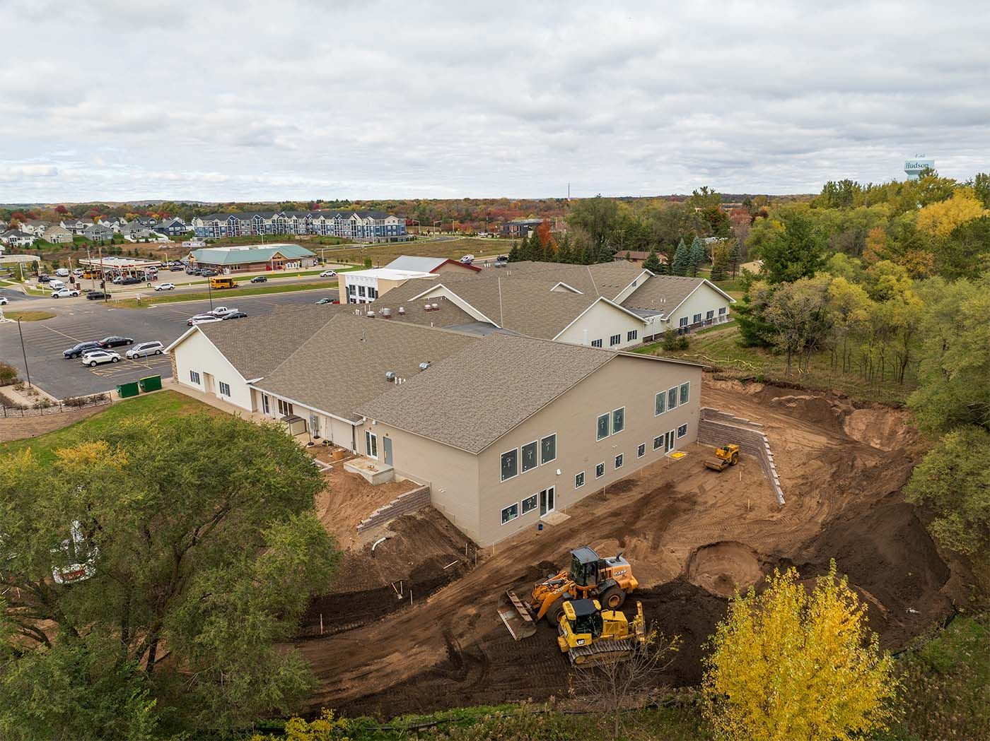 Aerial view of a light-colored building under construction; earthmoving equipment on the hillside.