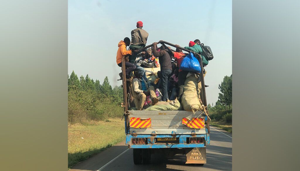 Truck overloaded with people and luggage on a road, driving forward.