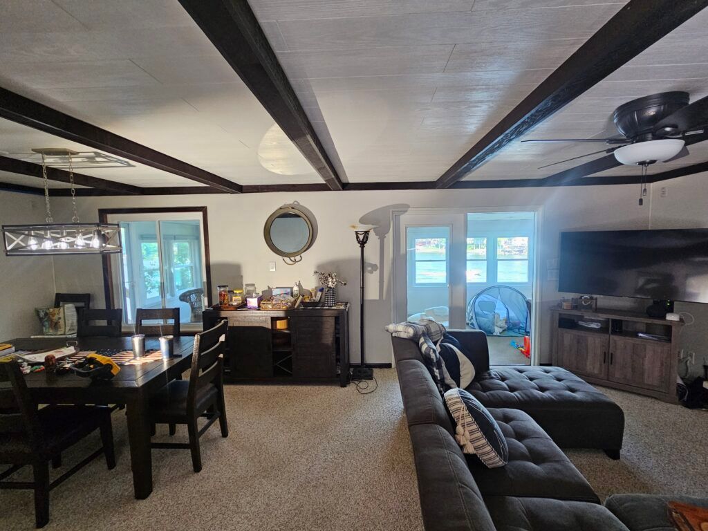 Living room with dark beams on the ceiling, a dining table, sectional couch, and tv.