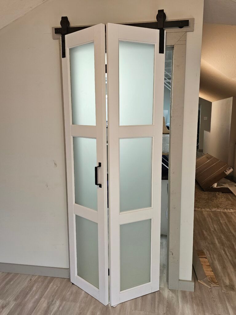 White bi-fold door with frosted glass panels, black hardware, installed on a sliding track.