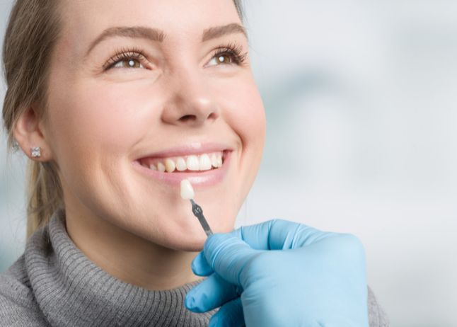 Woman smiling as dentist holds tooth veneer, indoors.