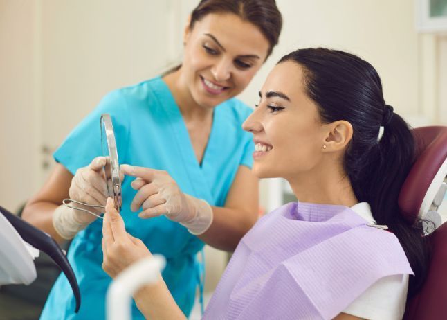 Dentist showing a patient her teeth with a mirror in a dental office.